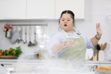 down syndrome teenage girl throwing and sprinkling white flour for making a bread or cooking food...