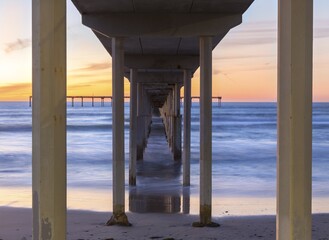 View Under Ocean Beach Pier Wooden Structure with Distant Orange Color Sunset Sky on Horizon in San Diego, Southern California