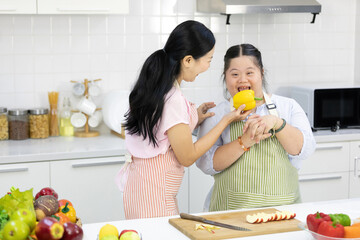 mother feeding yellow pepper to down syndrome teenage girl or her daughter in the kitchen