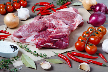 Close-up of large piece of fresh pork meat on kitchen table surrounded by fresh vegetables. Healthy food. Selective focus.