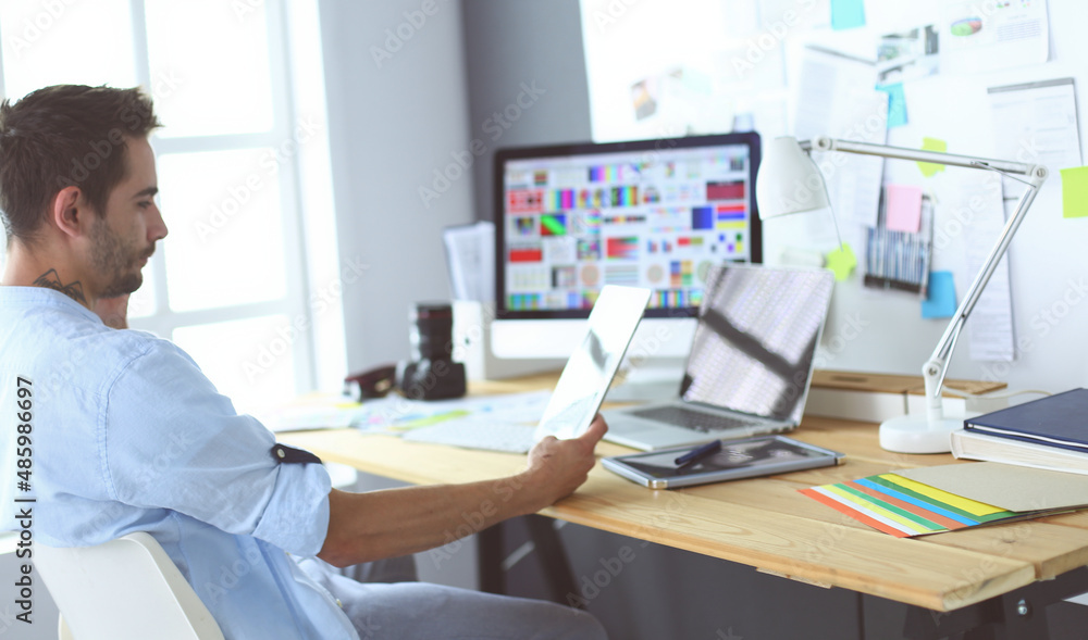 Poster portrait of young designer sitting at graphic studio in front of laptop and computer while working o