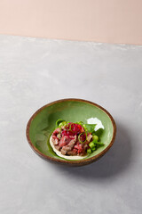 Appetizer - roast beef with sauce, cucumber and onion in ceramic bowl. Roast beef in modern ceramic dishware. Handmade dinner plate. Modern food in handmade dishware.