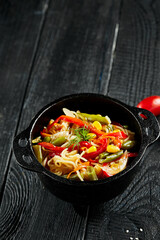 Vegetarian stir fried noodles on dark background. Asian vegan pasta on wok. Veggie wok on black wooden table. Spaghetti with vegetables on chinese style. Thai food menu..