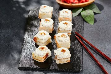 Maki sushi on dark slate. Unagi maki with eel. Sushi roll with eel fish, cream cheese and unagi sauce. Style concept japanese menu with black background, leaves and hard shadow.