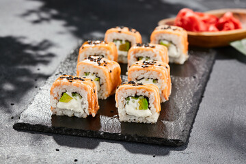 Maki sushi on dark slate. Hot philadelphia maki with baked salmon. Sushi roll with grilled salmon, cream cheese and avocado. Style concept japanese menu with black background, leaves and hard shadow.