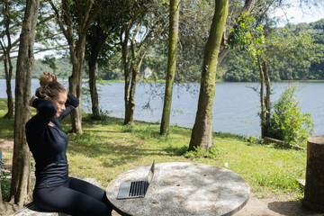 Young woman using a laptop at day time with a green park in the background. High quality photo