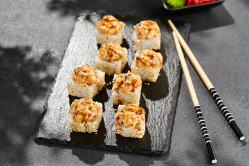 Baked Maki sushi on dark slate. Hot unagi maki with eel. Sushi roll with baked eel, cheese and unagi sauce topped. Style concept japanese menu with black background, leaves and hard shadow.