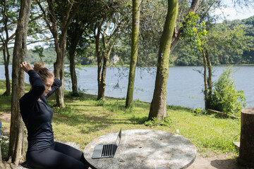 Fototapeta premium Young woman using a laptop at day time with a green park in the background. High quality photo