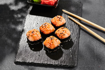 Baked Maki sushi on dark slate. Hot unagi maki with tobiko. Sushi roll with baked cheese, masago and unagi sauce topped. Style concept japanese menu with black background, leaves and hard shadow.