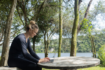 Young woman using a laptop at day time with a green park in the background. High quality photo