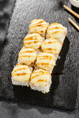 Baked Maki sushi on dark slate. Hot cheese maki with unagi sauce. Sushi roll with baked cheese and unagi sauce topped. Style concept japanese menu with black background, leaves and hard shadow.