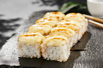 Baked Maki sushi on dark slate. Hot cheese maki with unagi sauce. Sushi roll with baked cheese and unagi sauce topped. Style concept japanese menu with black background, leaves and hard shadow.