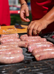 manos acomodando salchichas en el asador , para cocinarlas al carbón en un día soleado  