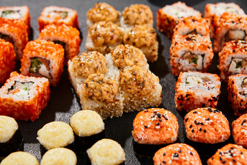 Maki sushi set on dark background. Maki set with variety rolls. Composition from sushi rolls and baked maki . Style concept sushi menu with black background, leaves and hard shadow.
