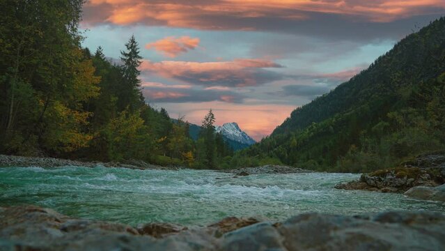 Scenic mountain river cinemagraph in the Austrian alps with a vibrant evening sky, close to the German border in autumn. The water is rushing along colorful fall trees. 4K UHD seamless video loop.