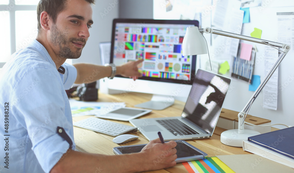 Poster portrait of young designer sitting at graphic studio in front of laptop and computer while working o