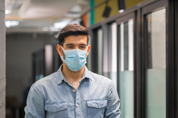 Fototapeta na wymiar Young businessman wear protection face mask against coronavirus standing in office