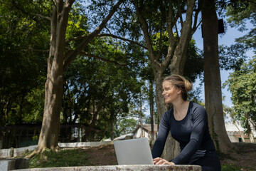 Fototapeta premium Young woman using a laptop at day time with a green park in the background. High quality photo