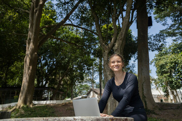 Young woman using a laptop at day time with a green park in the background. High quality photo