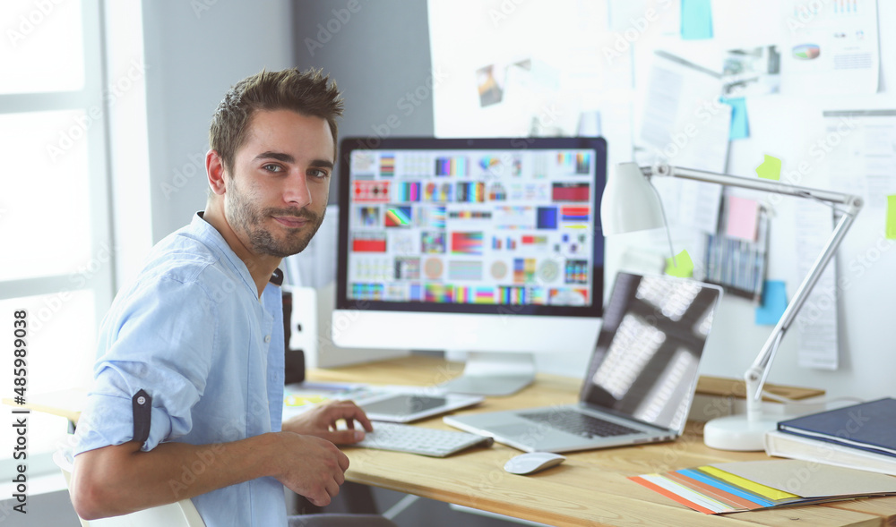Poster portrait of young designer sitting at graphic studio in front of laptop and computer while working o