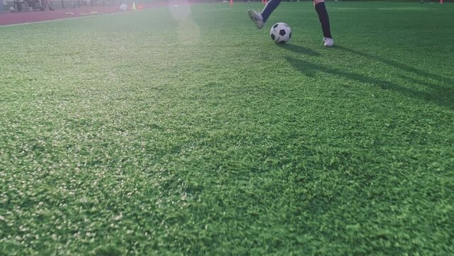 SLOW MOTION - Boy trains professionally on a football field with a ball. Training with a ball on football pitch while sunset. Active child makes a feint with football on a green field. Sport concept