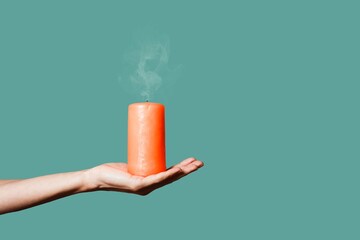 female hand holding extinguished aroma candle on her palm. Orange candle with fading smoke