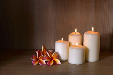 Burning candles and beautiful plumeria flowers on a wooden floor.