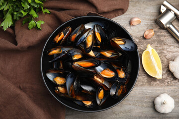 Bowl of delicious cooked mussels with parsley, garlic and lemon on wooden table, flat lay