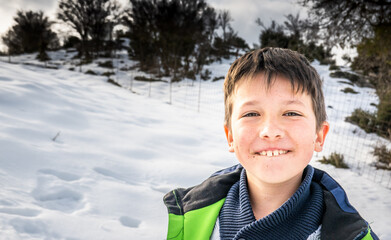 Happy little boy standing in snowy field