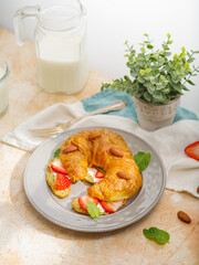 French breakfast. Croissant with fresh strawberries, almonds on a plate, milk and decor - indoor flower on a white background. Menu design, restaurant, hotel, cafe. Light background.