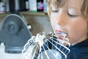 Close up of boy licking whipped cream from wire whisk