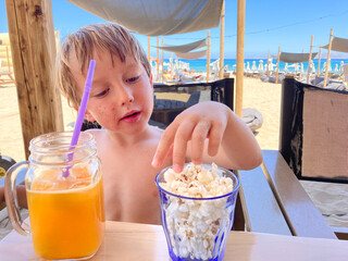 Boy drinking juice and eating popcorn at beach