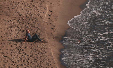 Adult man in jeans sitting on beach. Cabo de Gata Nature Park, Almeria, Spain