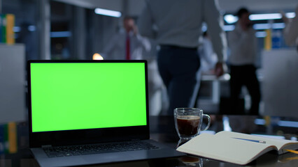 Fucus on laptop with green screen, coffee cup and notebook on office desk. Businesspeople work