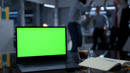 Focus on laptop with green screen. Colleagues dance and have fun on blurred background