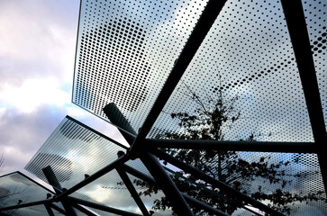 Bicycle parking shelter with glass roof with dotted print. Construction from bent gray tubes into...