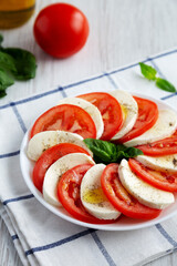 Homemade Caprese Salad with Mozzarella, Tomato and Basil on a white plate, side view.