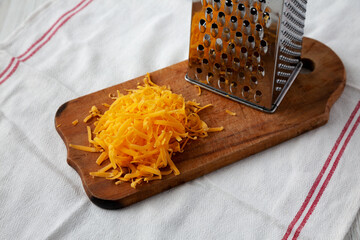 Shredded Sharp Cheddar Cheese on a rustic wooden board, side view.