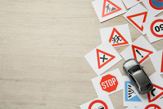 Many different road sign cards and toy car on wooden table, flat lay with space for text. Driving school