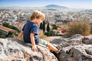 Little boy sitting on rock against cityscape