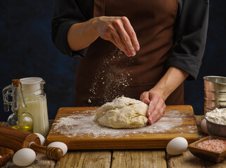 The chef prepares the dough on a wooden board. dark background. Sprinkle the dough with flour. Levitation. Recipes for making dough products - pizza, bread, pie, pasta. Home and restaurant cuisine.