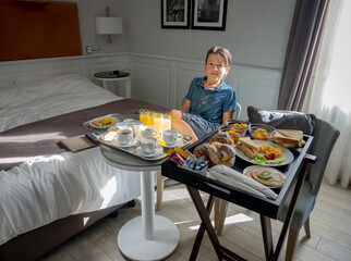 Little boy sitting beside freshly delivered breakfast in hotel room