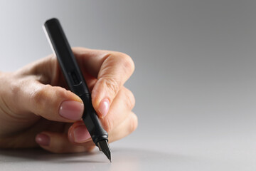 Person holding black feather pen, sharp tip, tool for writing