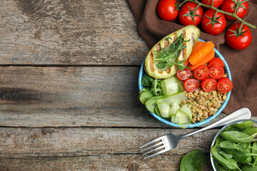 Delicious lentil bowl with avocado, tomatoes, carrot and cucumber on wooden table, flat lay. Space for text