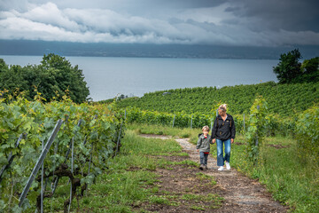 Mother with son walking on trail through green vineyard