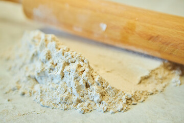 Grey flour and a rolling pin for dough. Raw products for the preparation of flour products. Organic food.