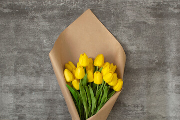 Spring flowers, a tulip on a gray background. Yellow beautiful tulips with a space for text. A bouquet of tulips wrapped in kraft paper