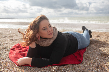 Fototapeta na wymiar Beatuful woman with over weight body walking in the beach, The plus size model wearing jeans, the warm knitted blanket and sweater. the wind in the bich have fun with hairs