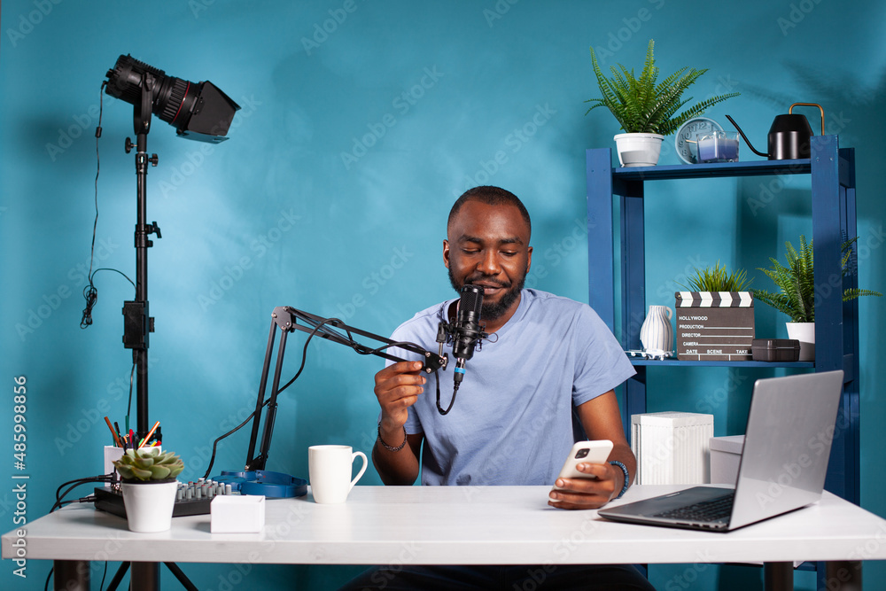 Poster vlogger holding smartphone looking at screen reading questions from fans using microphone sitting at