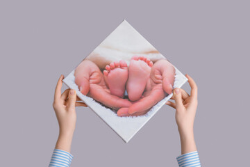 Women's hands hang a family photo of a newborn's legs printed on canvas on a gray wall
